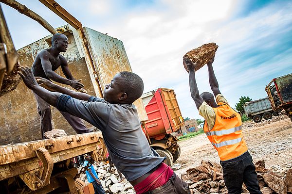 Stein für Stein verladen junge Männer den abgebauten Kalkfelsen zum Abtransport auf Lkw. 