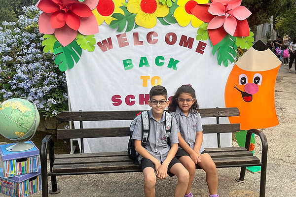die beiden Kinder von Nicole Zreineh sitzen auf einer Bank vor ihrer Schule