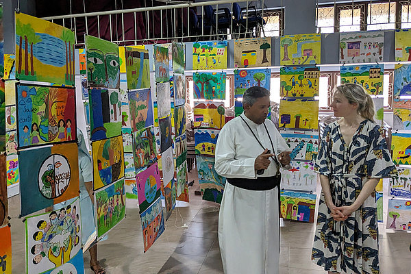Father Rohan und Franziska Eder (von links) schauen sich die Ausstellung zu Religion und Umwelt mit Beiträgen von 400 Kindern aus der Region an. Sie ist vom CSR initiiert, um mittels interreligiösem Dialog Frieden zu fördern.  Die Veranstaltung findet jährlich mit wechselnden Themen statt und wird unter anderem von AGIAMONDO unterstützt.